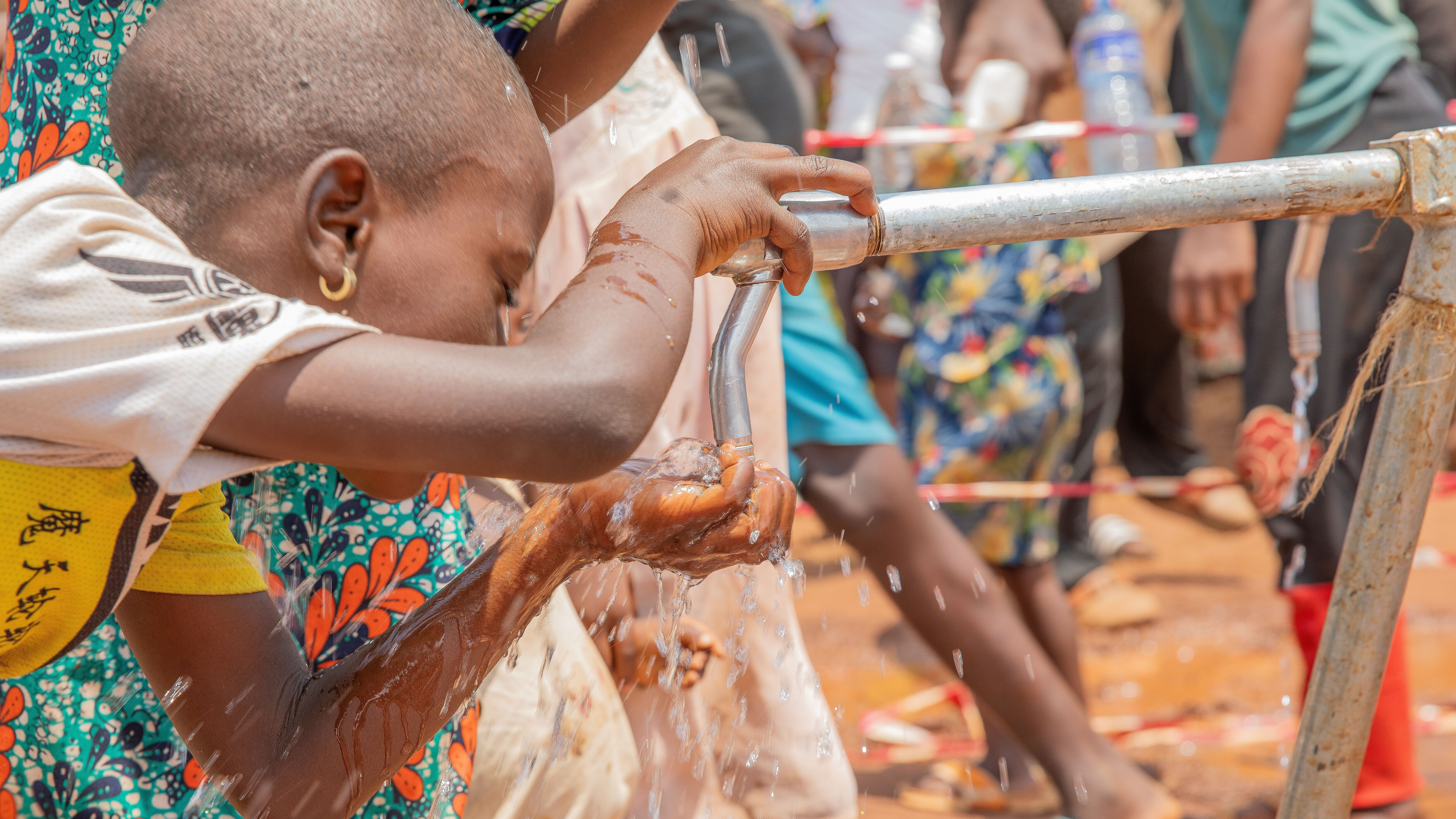 Ein Mädchen schöpft mit den Händen Wasser aus einem Wasserhahn