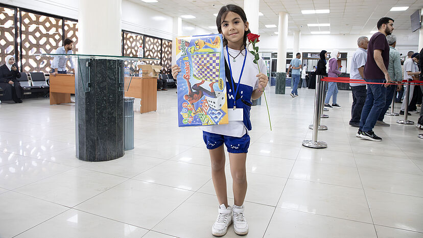 Ein kleines Mädchen seigt lächelnd ein Spiel und eine Blume