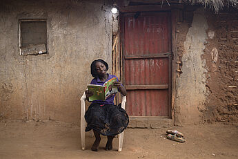 Ein Mädchen sitzt draußen vor einer Tür und liest ein Buch