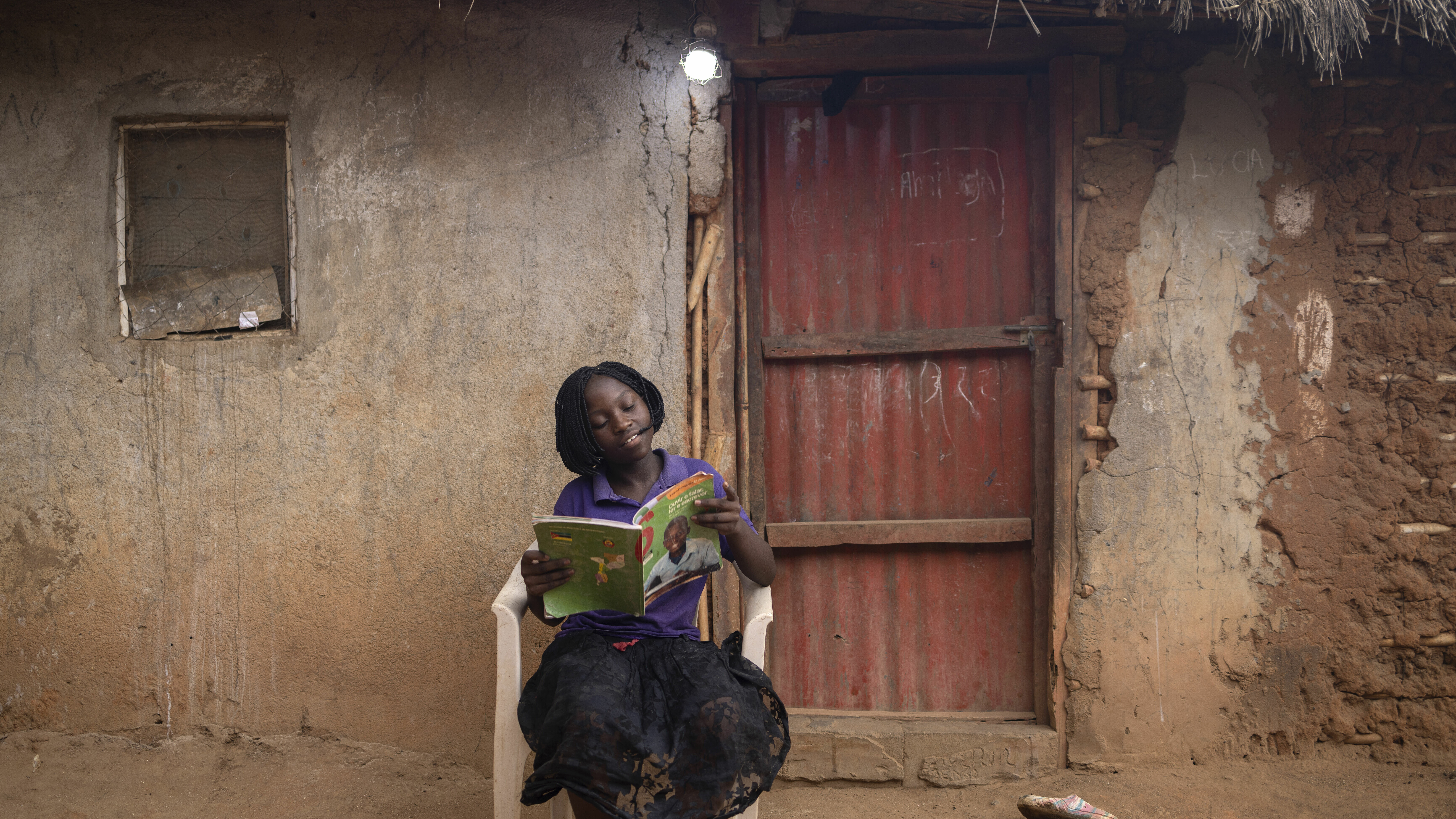 Ein Mädchen sitzt draußen vor einer Tür und liest ein Buch