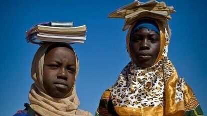 Zwei Flüchtlingsmädchen tragen ihre Lernmaterialen auf dem Kopf