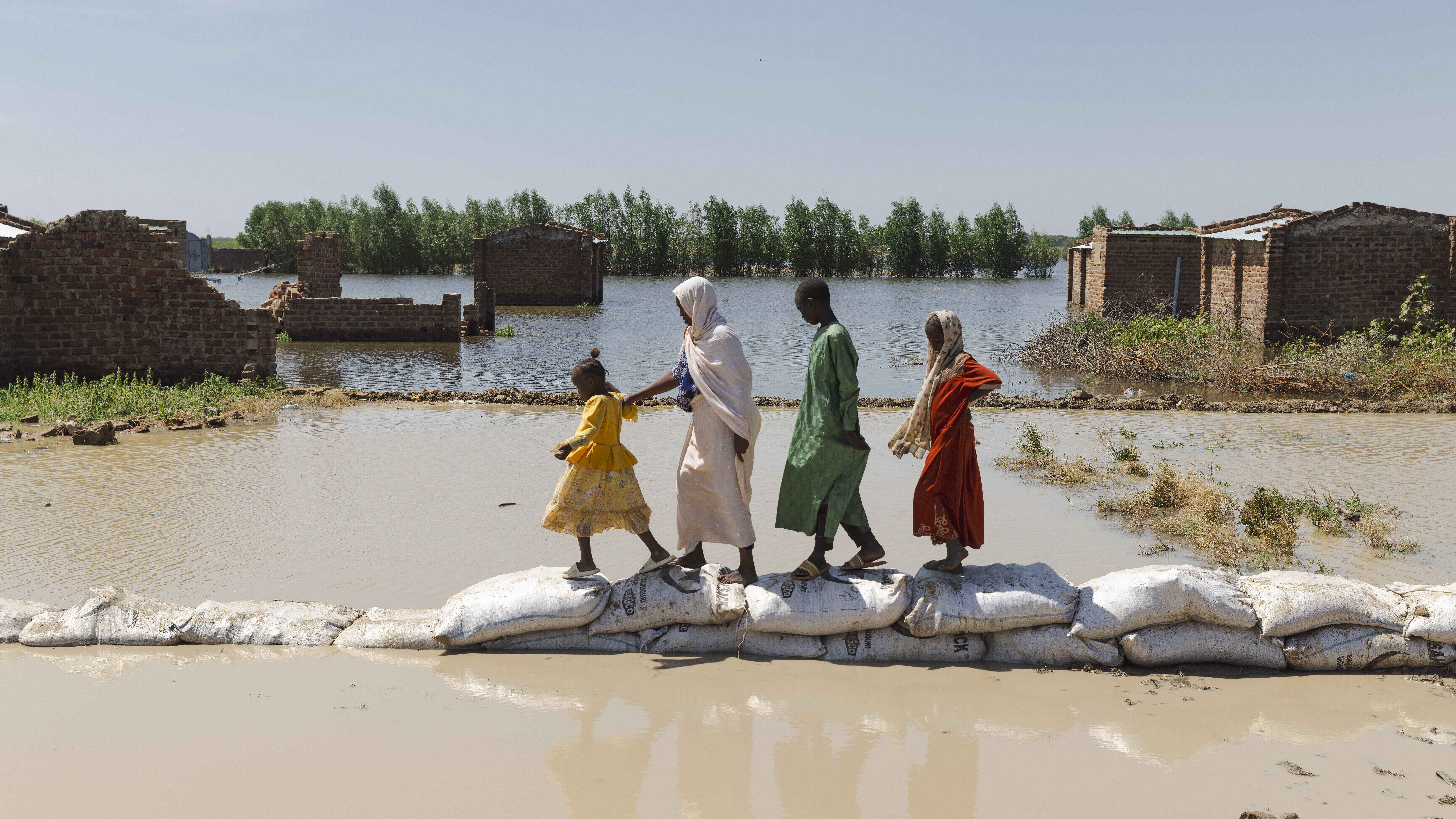 Frau mit 3 Kindern bahnt sich den weg über Sandsäcke mitten in der Flut