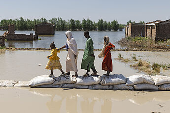 Eine Mutter und drei Kinder bahnen sich einen Weg über Sandsäcke inmitten von Fluten