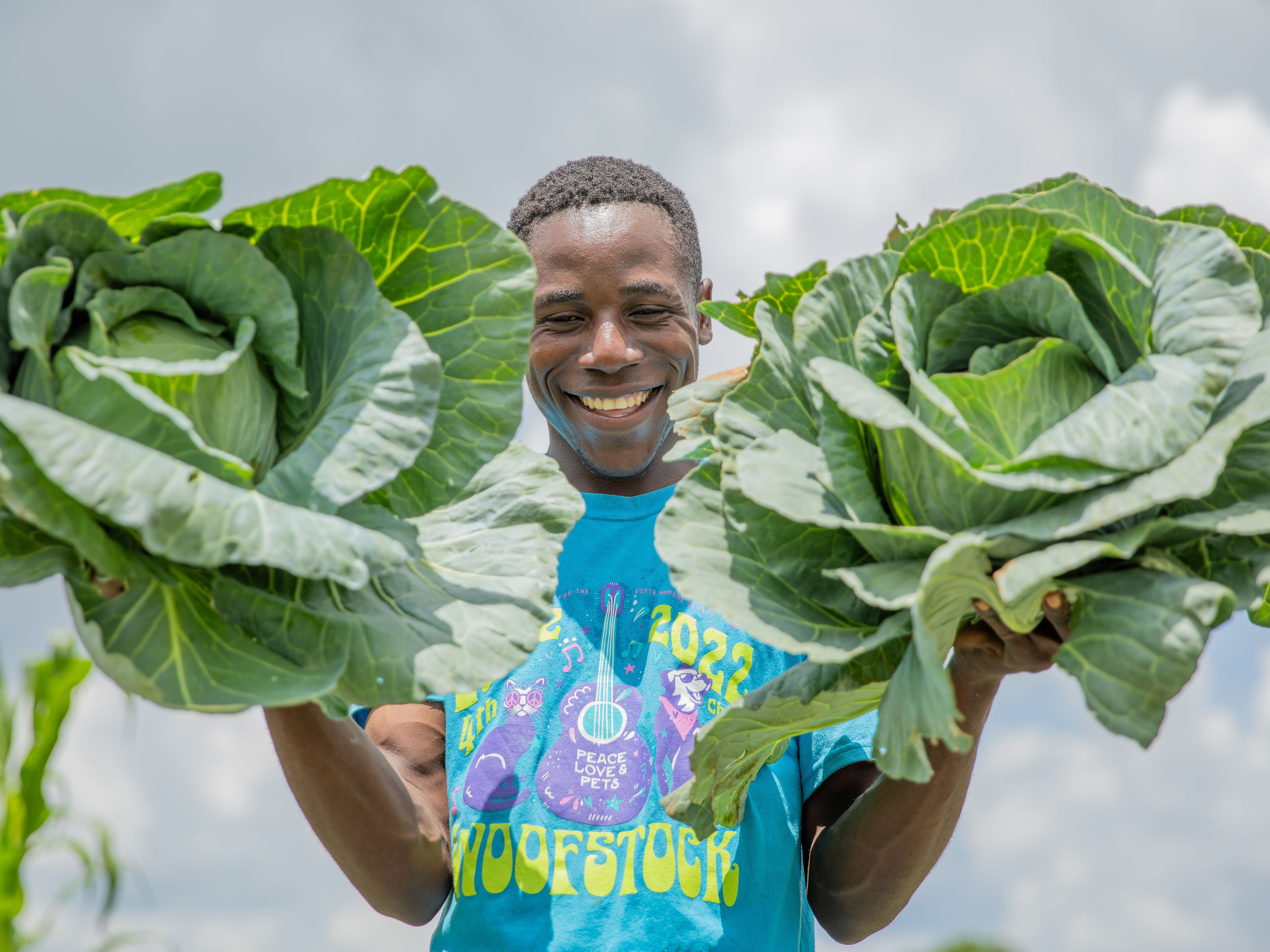 Junger Mann auf einer Plantage, grinst mit frischer Ernte in  die Kamera