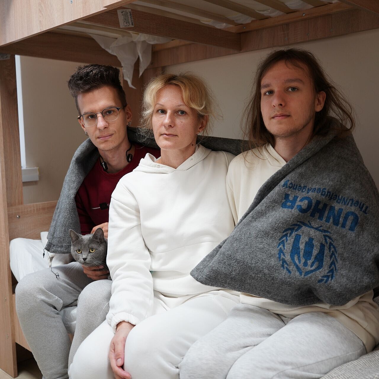 Frau sitzt auf Bett mit zwei erwachsenen Kindern rechts und links neben sich