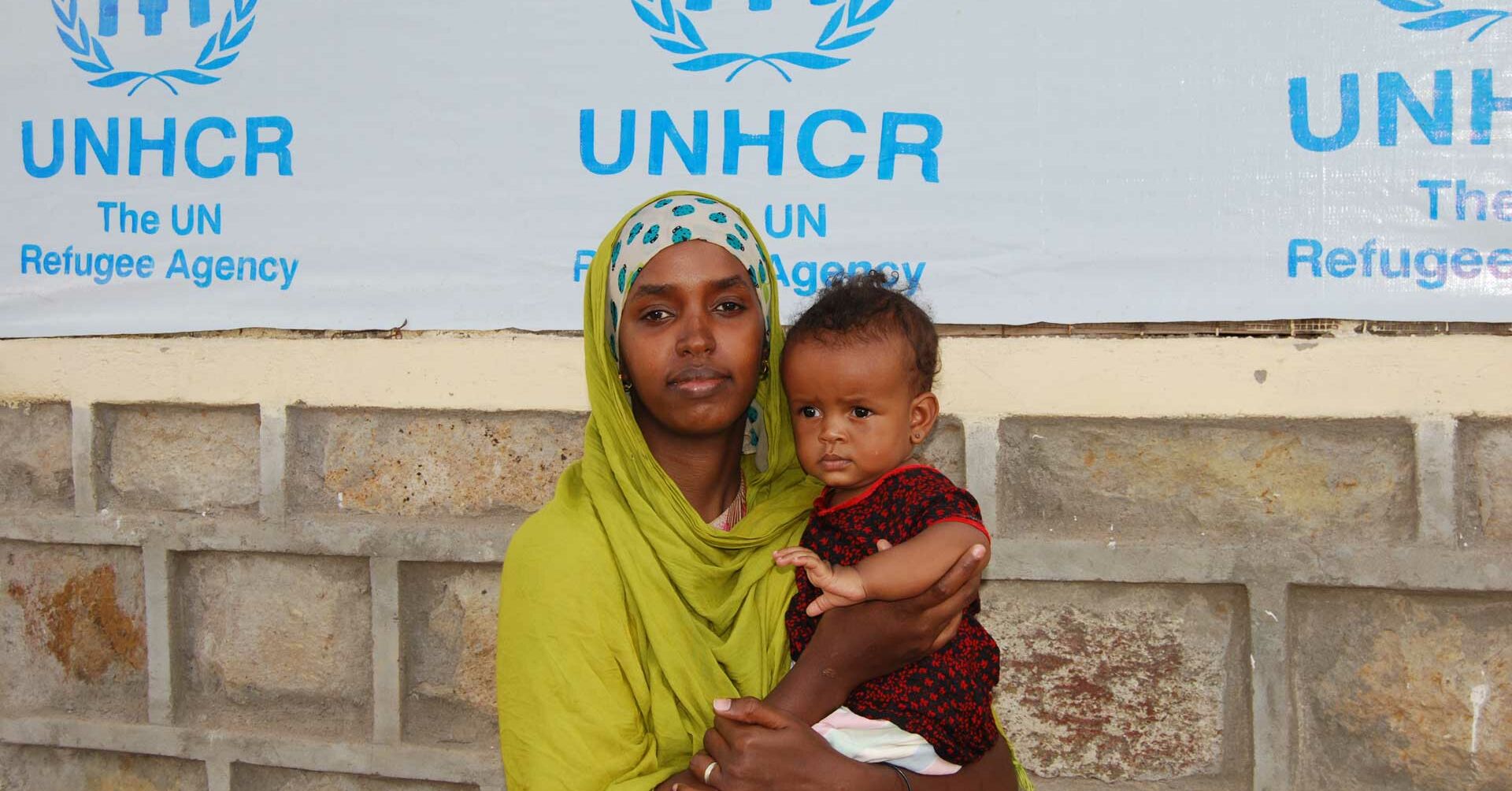 Frau mit Kind auf dem Arm, Hintergrund Plane mit UNHCR Logo Auslandshilfe.jpg
