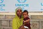 Frau mit Kind auf dem Arm, Hintergrund Plane mit UNHCR Logo