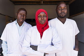 sudanesische medizinische Fachkräfte, zwei Pfleger und eine Ärztin, in ihrer Arbeitskleidung im Tschad nach der Flucht aus ihrer Heimat.