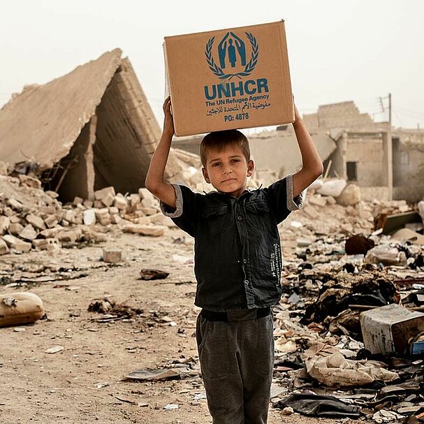 Junge mit UNHCR-Hilfspaket über dem Kopf