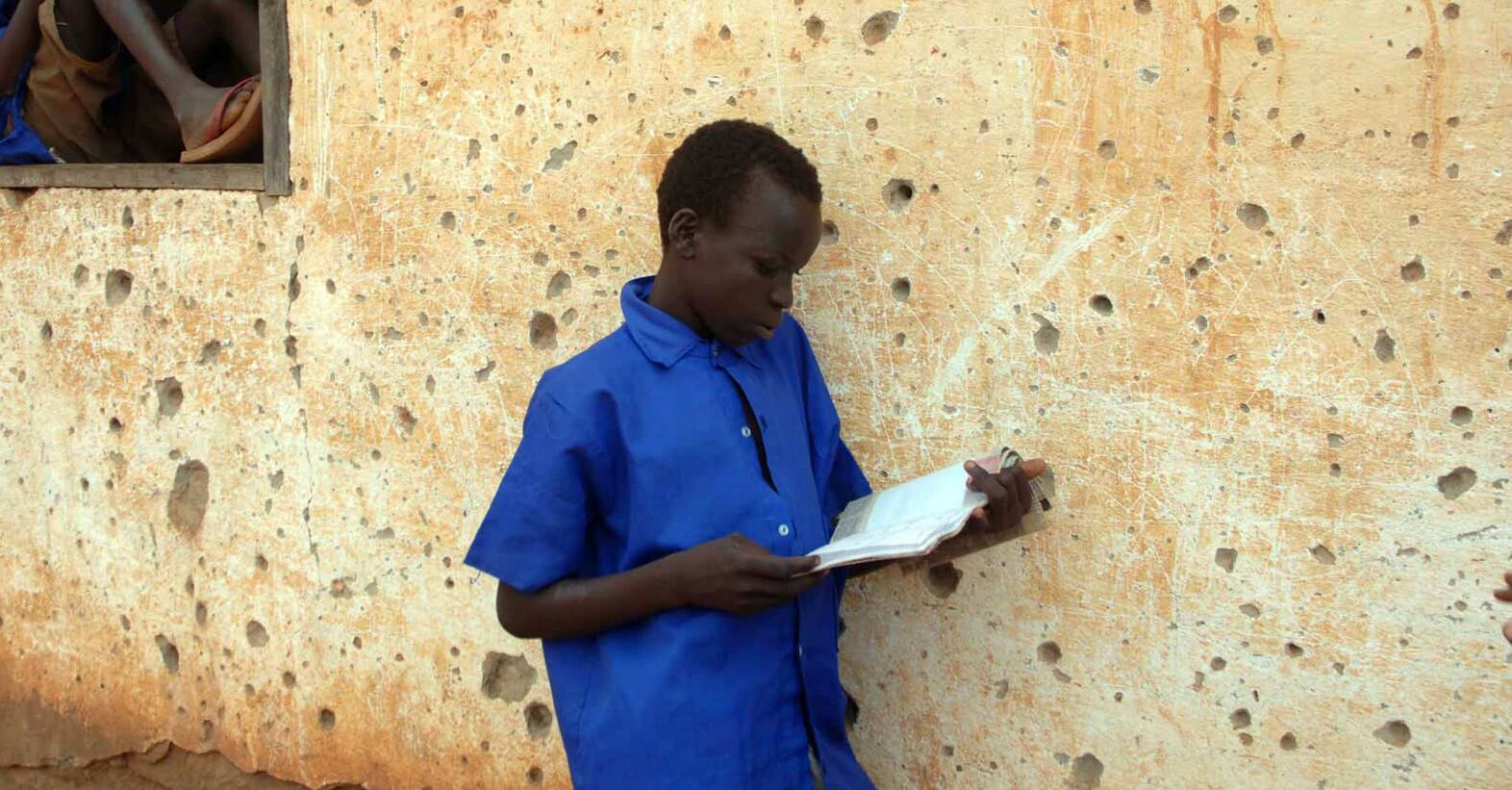 Junge liest Buch angelehnt an Hauswand, Bücher Junge Erwachsene  SudanBildung_1920x1080.jpg