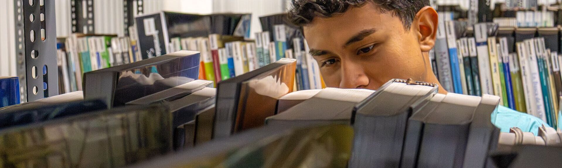 Ein Junge hinter einem Bücherregal am stöbern