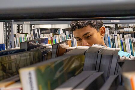 Junge steht hinter Bücherregal
