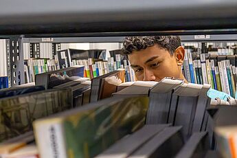 Junge steht hinter Bücherregal