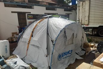 UNHCR-Zelt steht auf Straße zwischen zerstörten Häusern