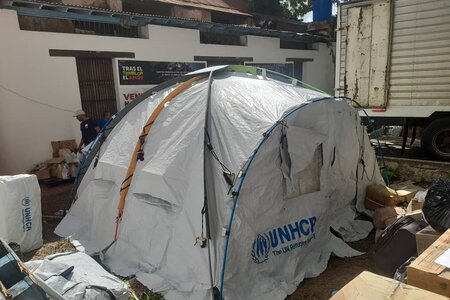 UNHCR-Zelt steht auf Straße zwischen zerstörten Häusern
