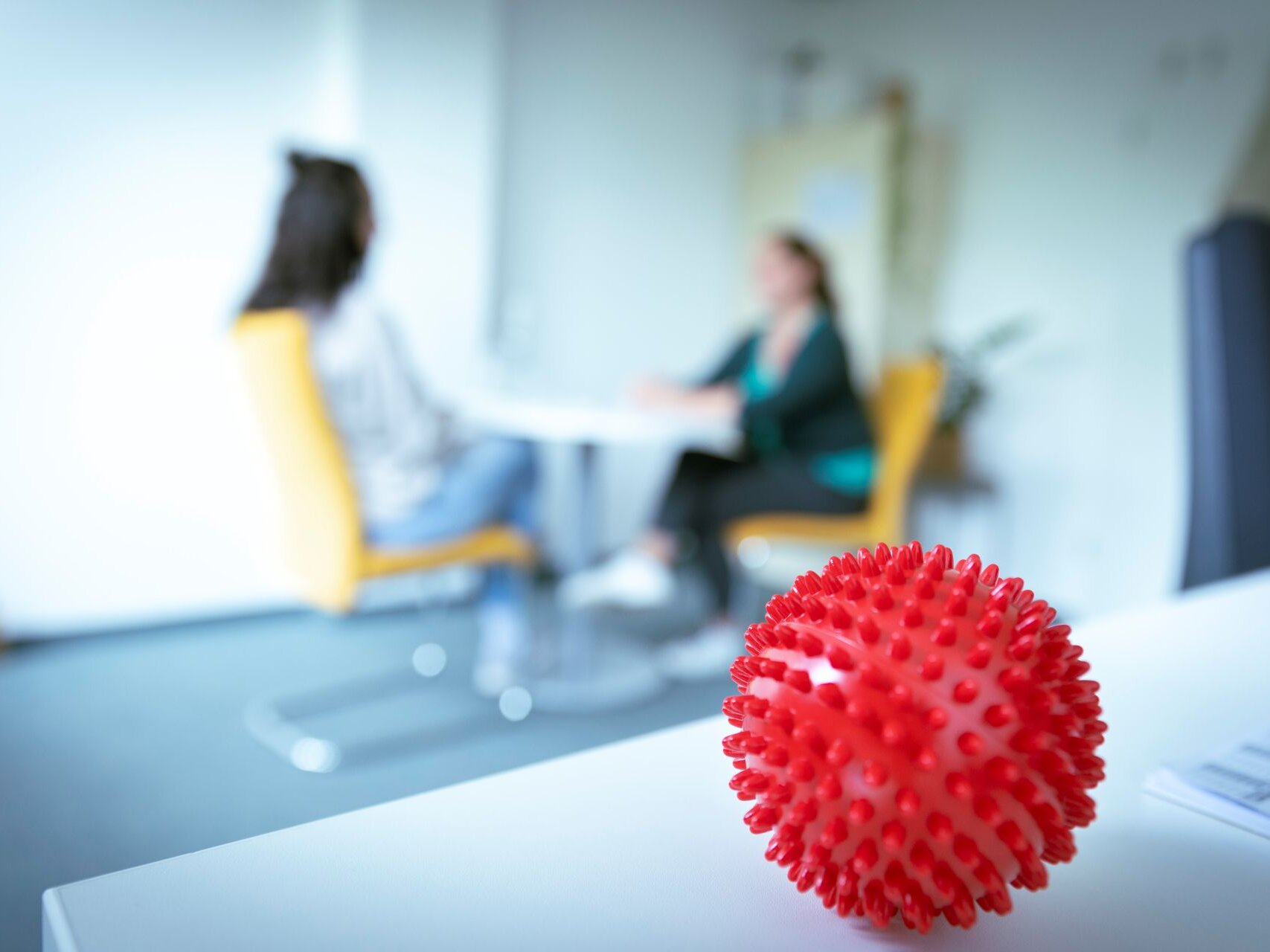 Ein verschwommenes zweier Menschen im Gespräch mit einem Therapieball im Fokus