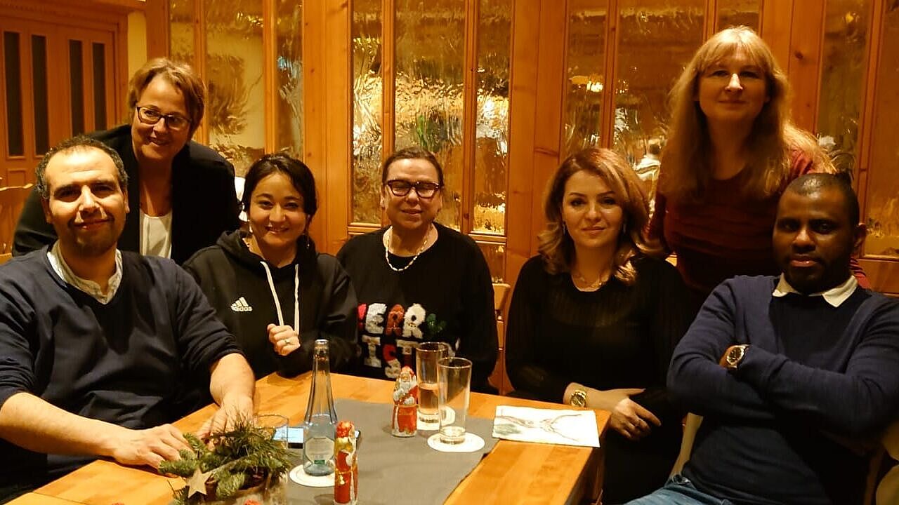 Mailka sitzt am Tisch mit sechs anderen Personen