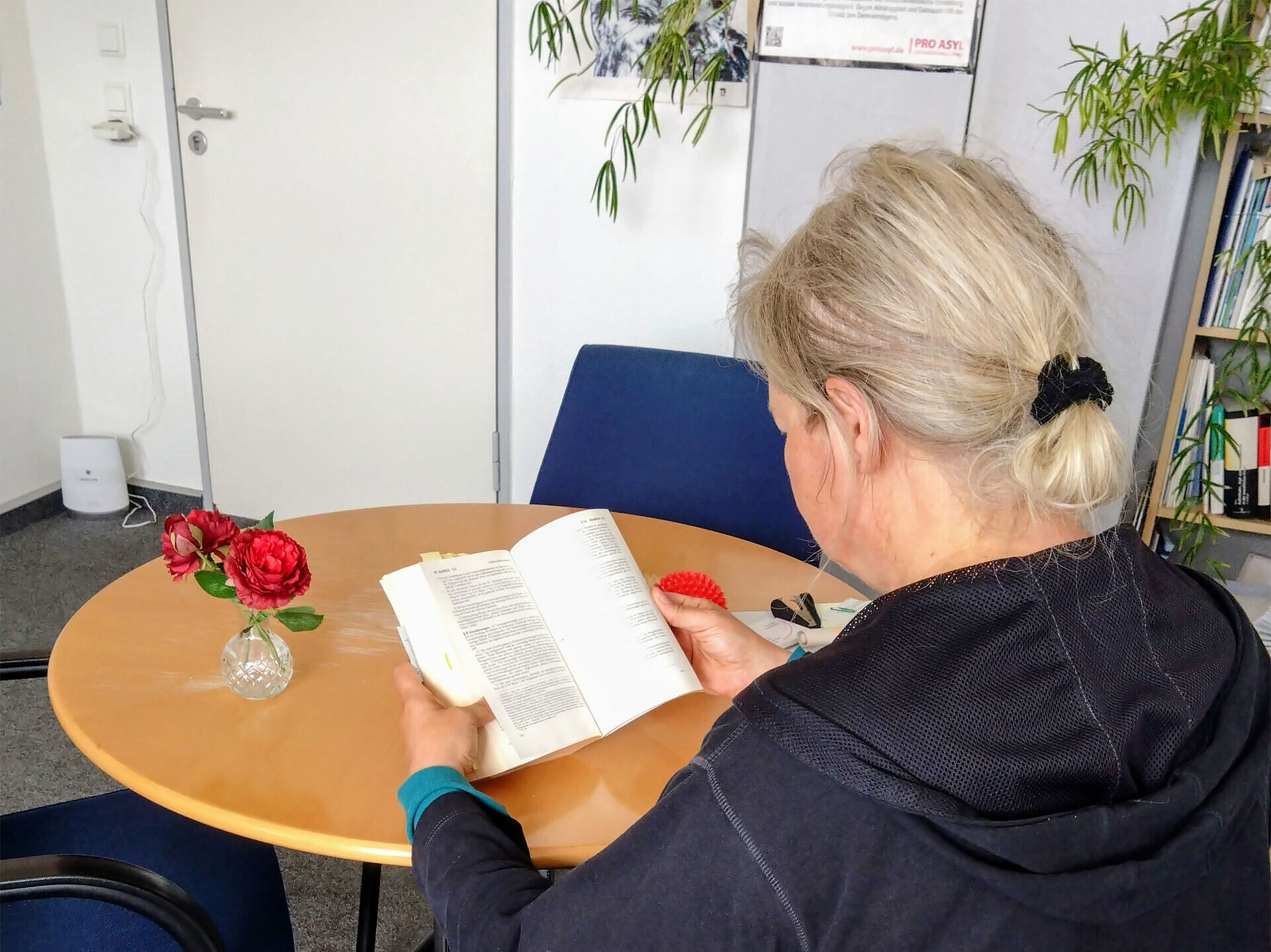 Eine von hinten fotografierte Frau, die lesend an einem Tisch sitzt.