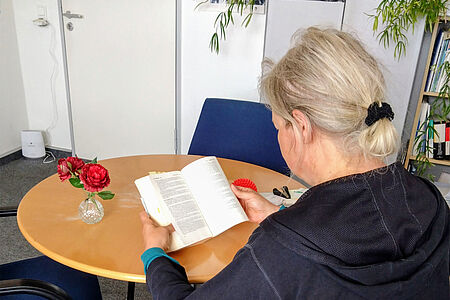 Frau von hinten sitzt lesend am Tisch