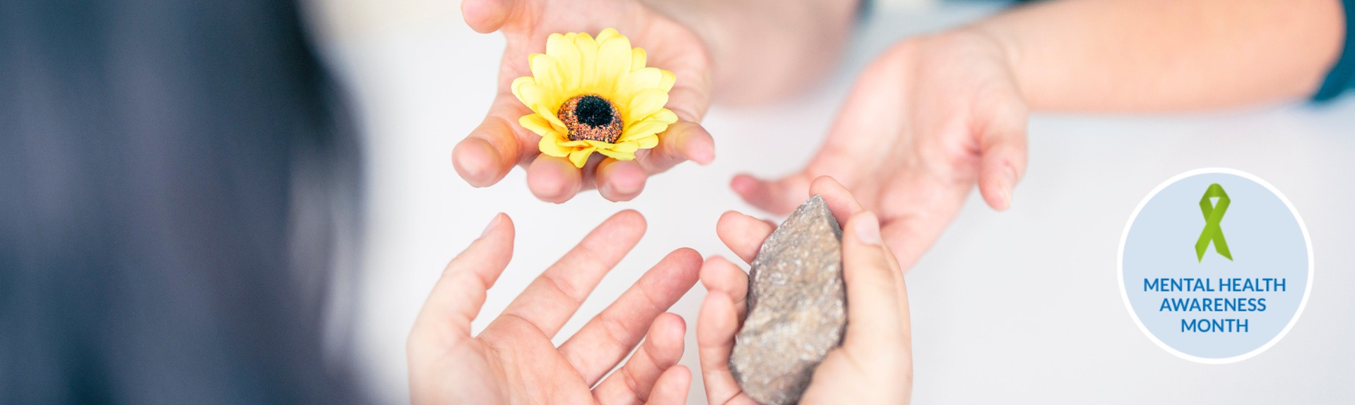 Zwei Paar Hände reichen sich einen Stein und eine Blume