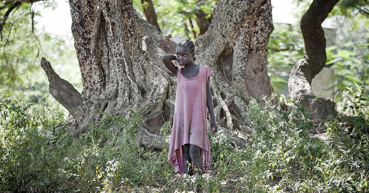Afrikanisches Mädchen steht in zerschlissenem roten Kleid in einem Wald. 56eab7810_1_.jpg