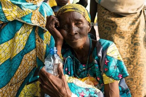 Alte Frau hockt auf dem Boen zwischen anderen Beinen
