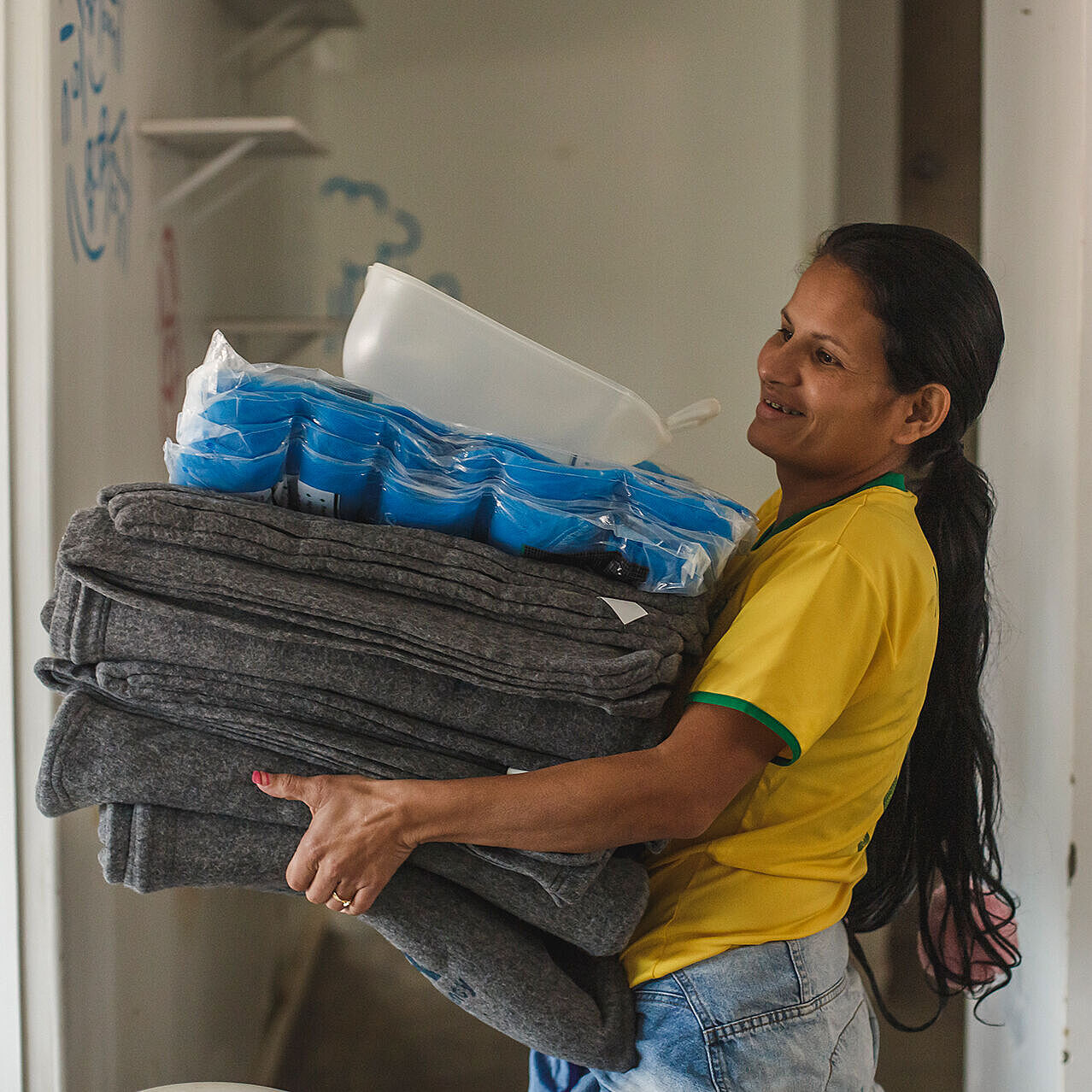 Frau trägt Hilfsgüterstpel mit Decken und Plastikplanen auf dem Arm