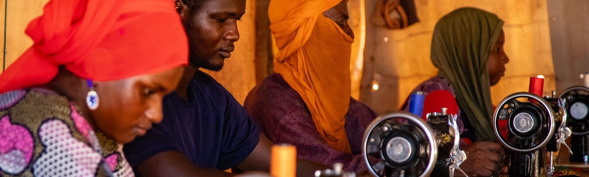 mehrere Menschen sitzen je an einer Nähmaschine