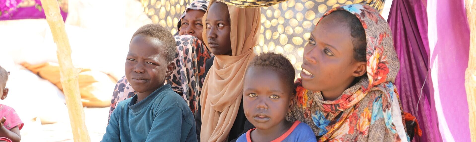 Gruppe von Frauen und Kindern sitzt unter einem selbstgebauten Unterstand
