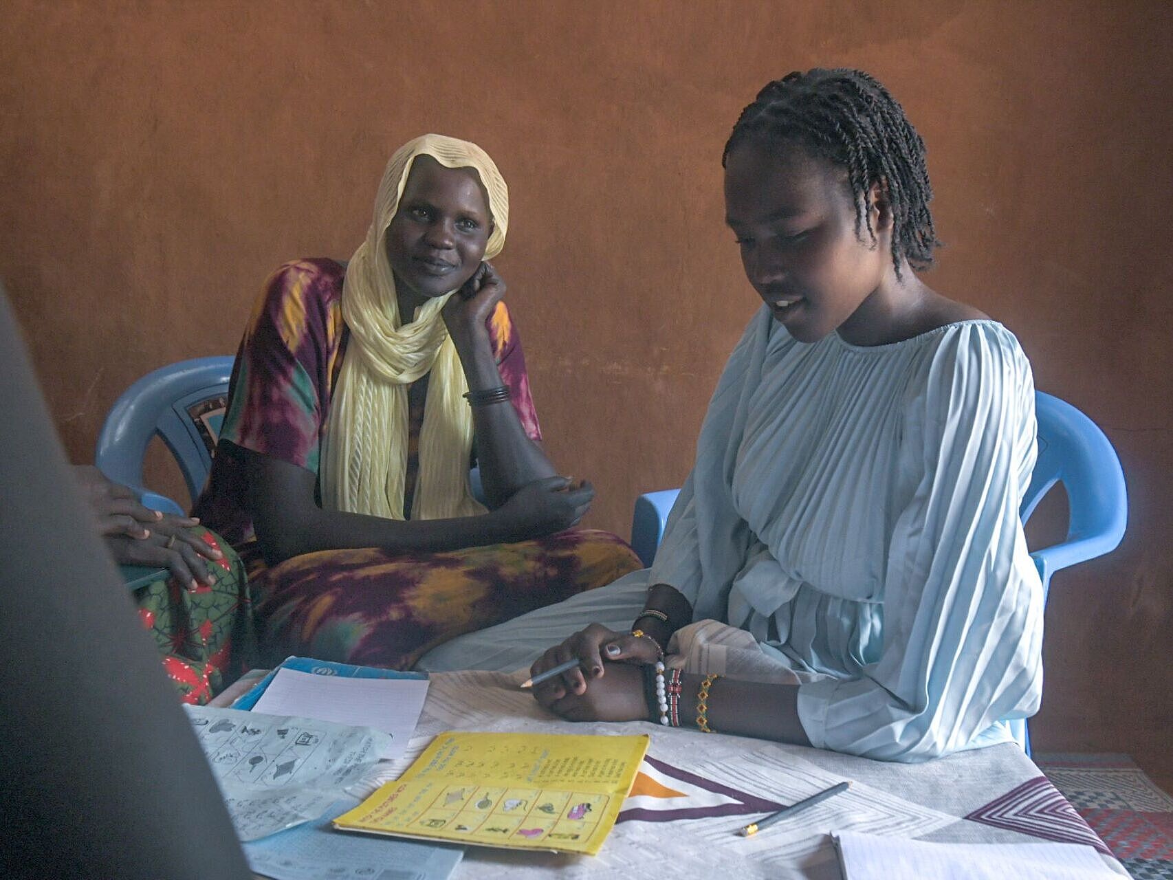 Ein Mädchen und eine Frau sitzen an einem Tisch mit Unterlagen und lernen