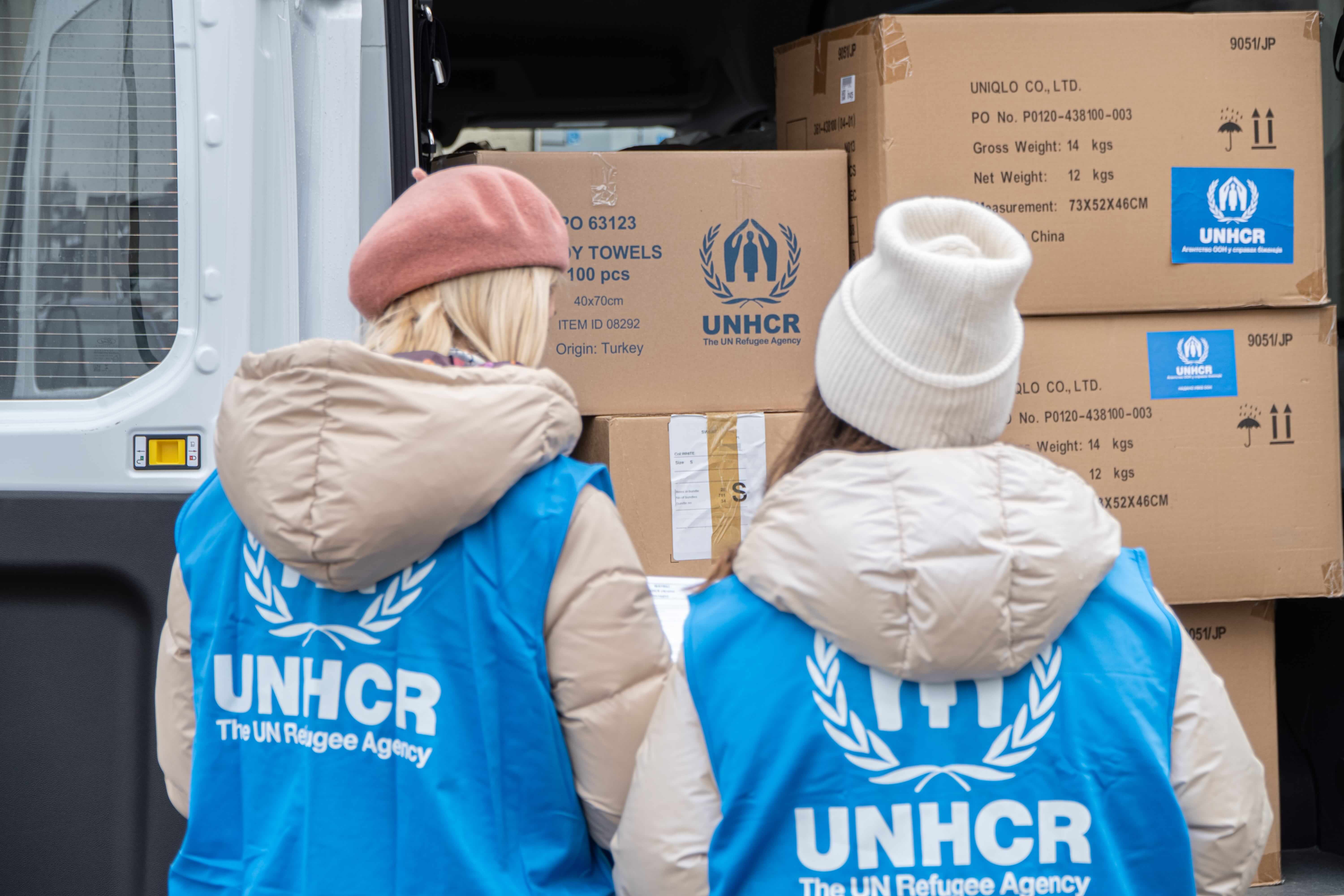 Mitarbeitende des UNHCR stehen vor verpackten Hilfsgütern