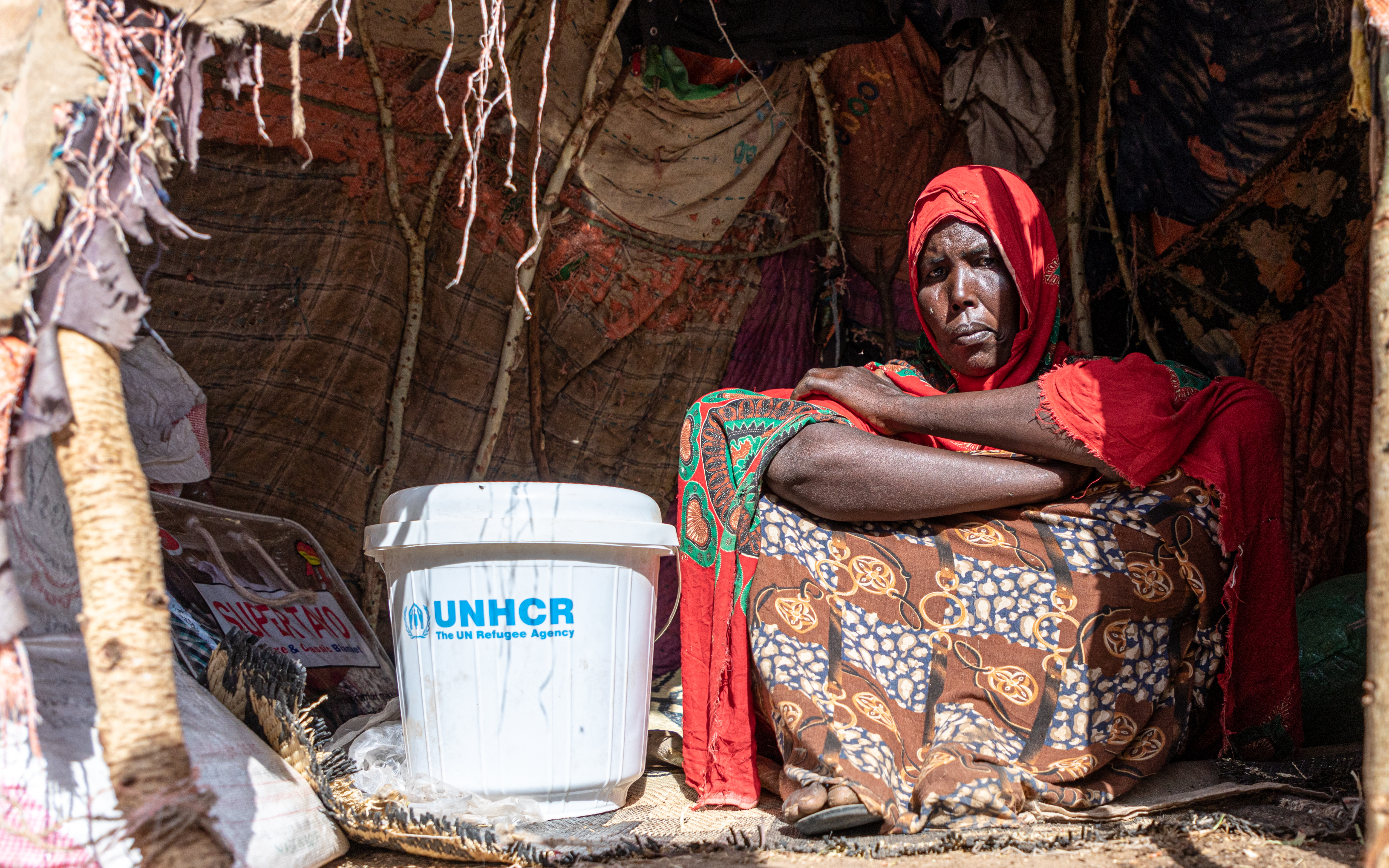 Eine Binnenvertriebene aus Äthiopien sitzt neben einem UNHCR-Eimer in einem Zelt